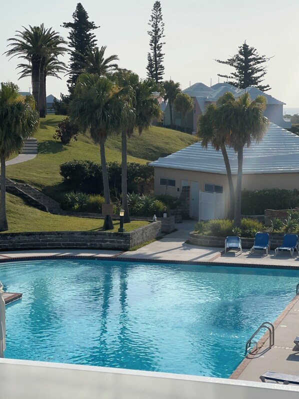 A swimming pool with lounge chairs, palm trees, and a building with a sloped roof.
