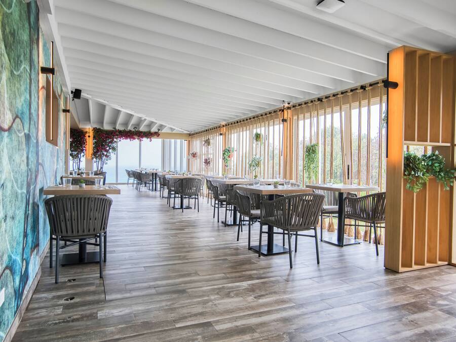 A spacious restaurant with wooden flooring, modern chairs, and large windows allowing natural light.