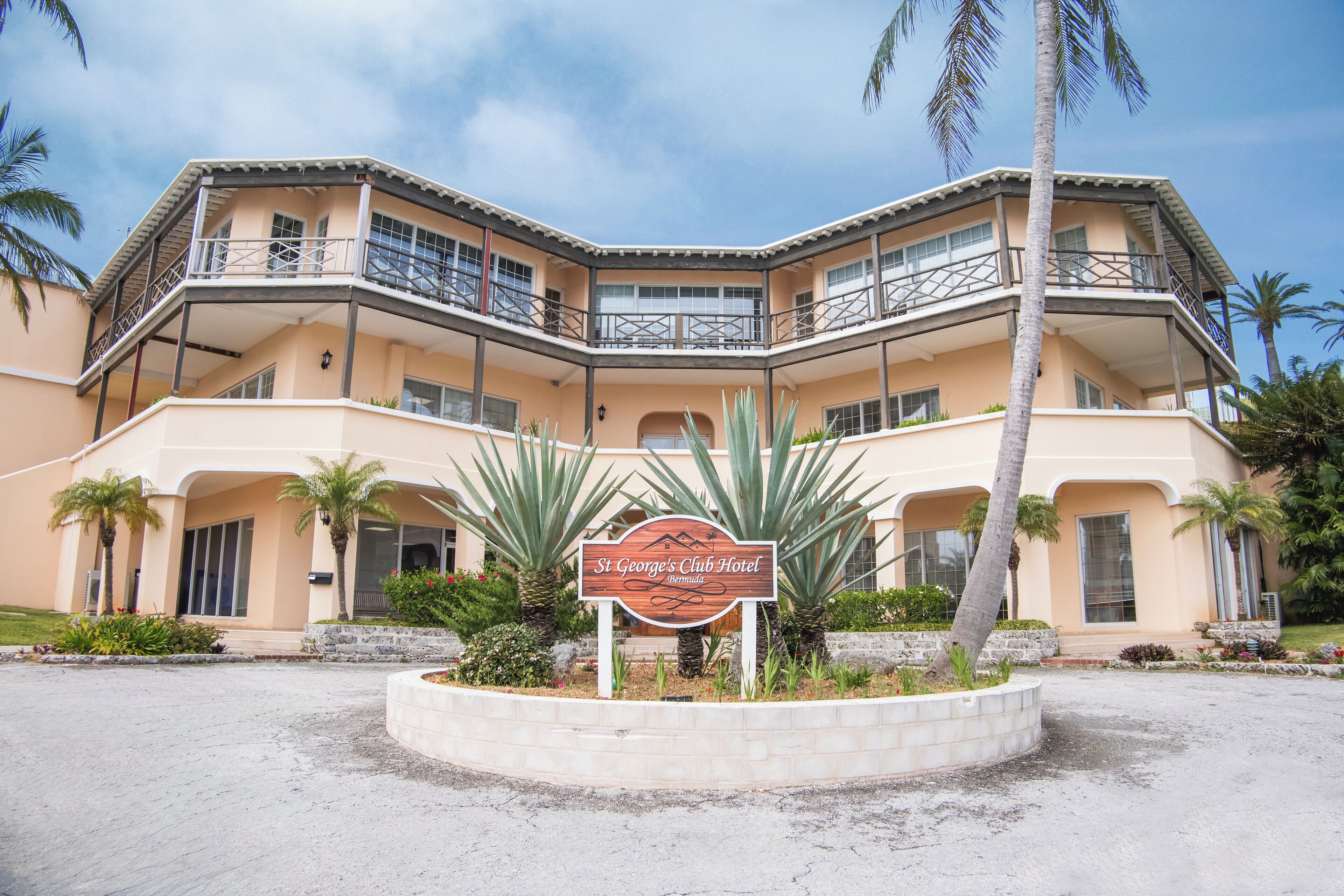 A multi-story hotel with a sign reading "St George's Club Hotel" surrounded by palm trees and a landscaped area.