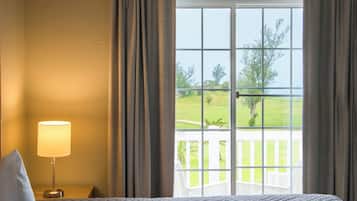 A hotel room with a bed, a nightstand with a lamp, and a view of a green landscape through a large window.