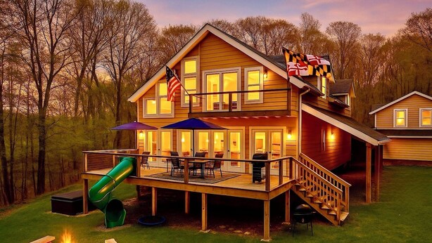 Ein zweistöckiges Holzhaus mit Terrasse, Sitzgelegenheiten im Freien, einer Rutsche und einem Feuerkorb.