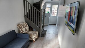 Un salon comprenant un canapé, un fauteuil à motifs, un escalier et une porte donnant sur une cuisine.