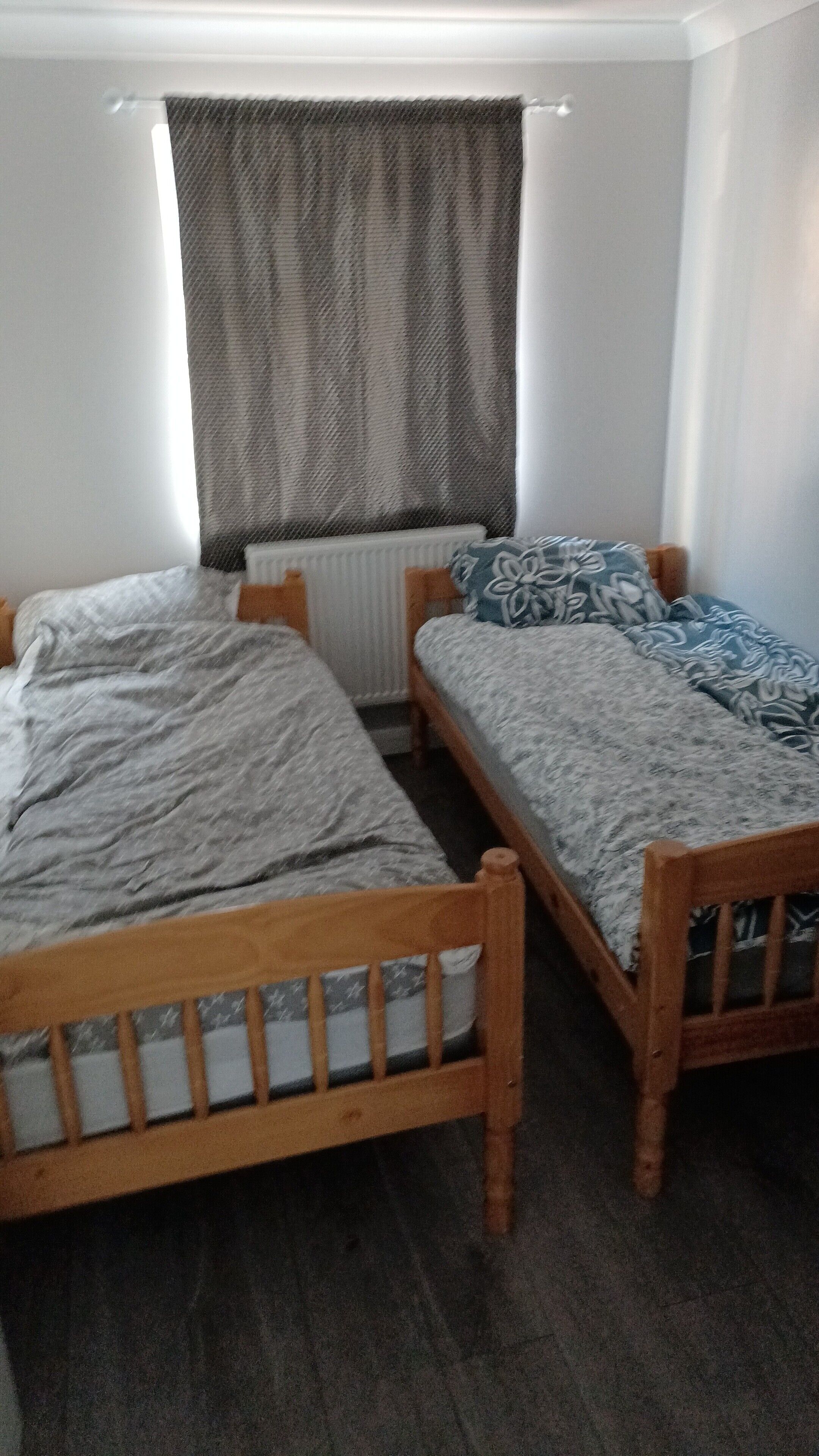 A room with two wooden beds, a window with a curtain, and a radiator.