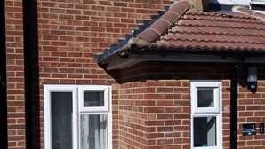 Une maison à deux étages, construite en briques, avec des fenêtres à cadre blanc, un toit en tuiles et une antenne parabolique.