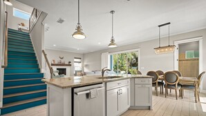A modern kitchen with a central island, a dining area with wooden chairs, and a staircase with teal steps. - 4 blocks from beach! spacious getaway w game room, outdoor kitchen. Kid-friendly (Jacksonville Beach)