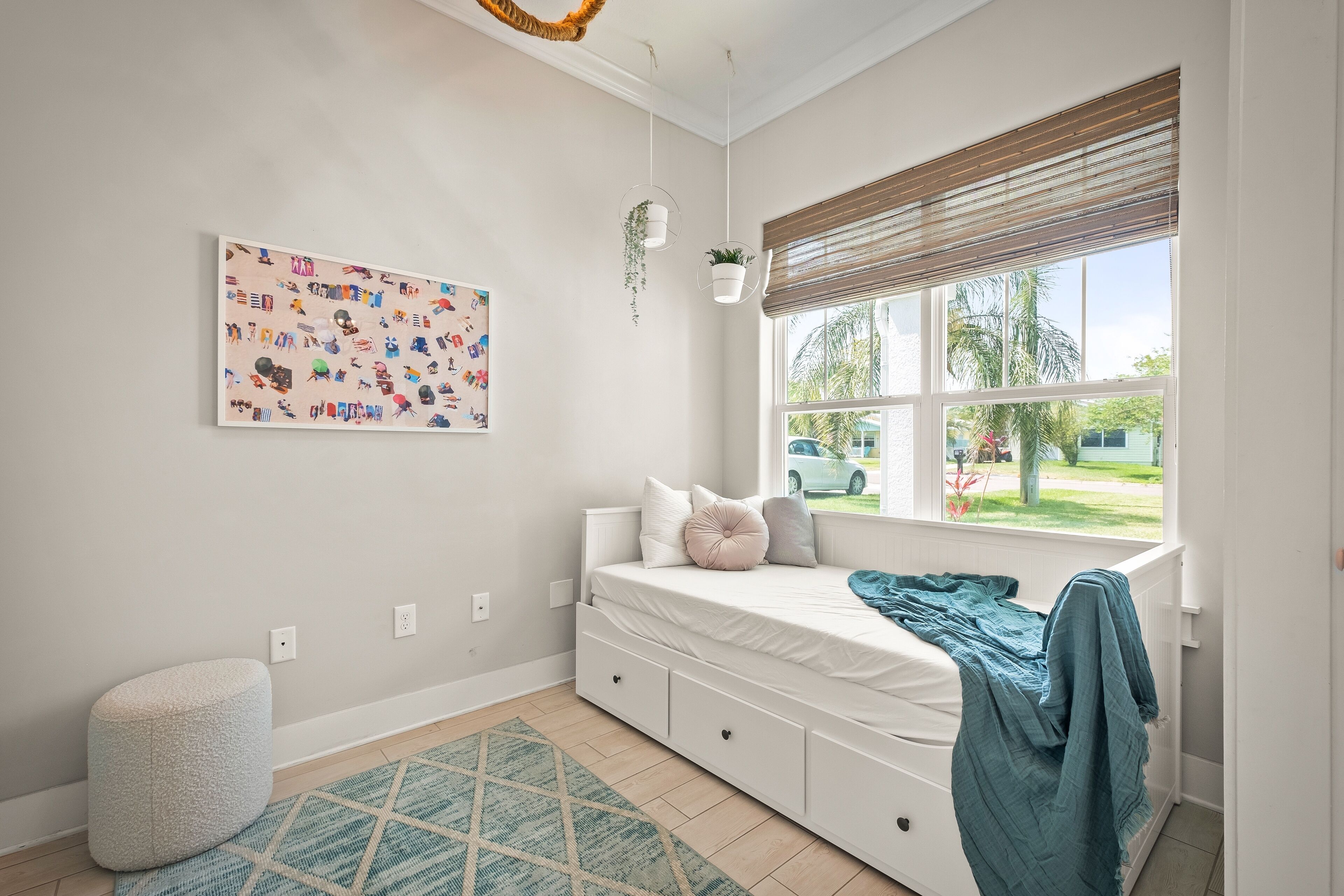 Une chambre à coucher avec un lit, une fenêtre avec des stores, une plante fixée au mur et un tapis à motifs géométriques.