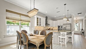 A spacious kitchen with white cabinetry, a central island, and a dining area with a wooden table and chairs. - 4 blocks from beach! spacious getaway w game room, outdoor kitchen. Kid-friendly (Jacksonville Beach)
