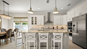 A modern kitchen with white cabinetry, a central island with bar stools, stainless steel appliances, and pendant lighting. - 4 blocks from beach! spacious getaway w game room, outdoor kitchen. Kid-friendly (Jacksonville Beach)
