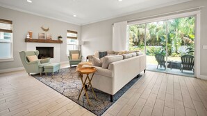 A spacious living room with a fireplace, a sofa, a coffee table, and a view of a lush garden through large sliding glass doors. - 4 blocks from beach! spacious getaway w game room, outdoor kitchen. Kid-friendly (Jacksonville Beach)