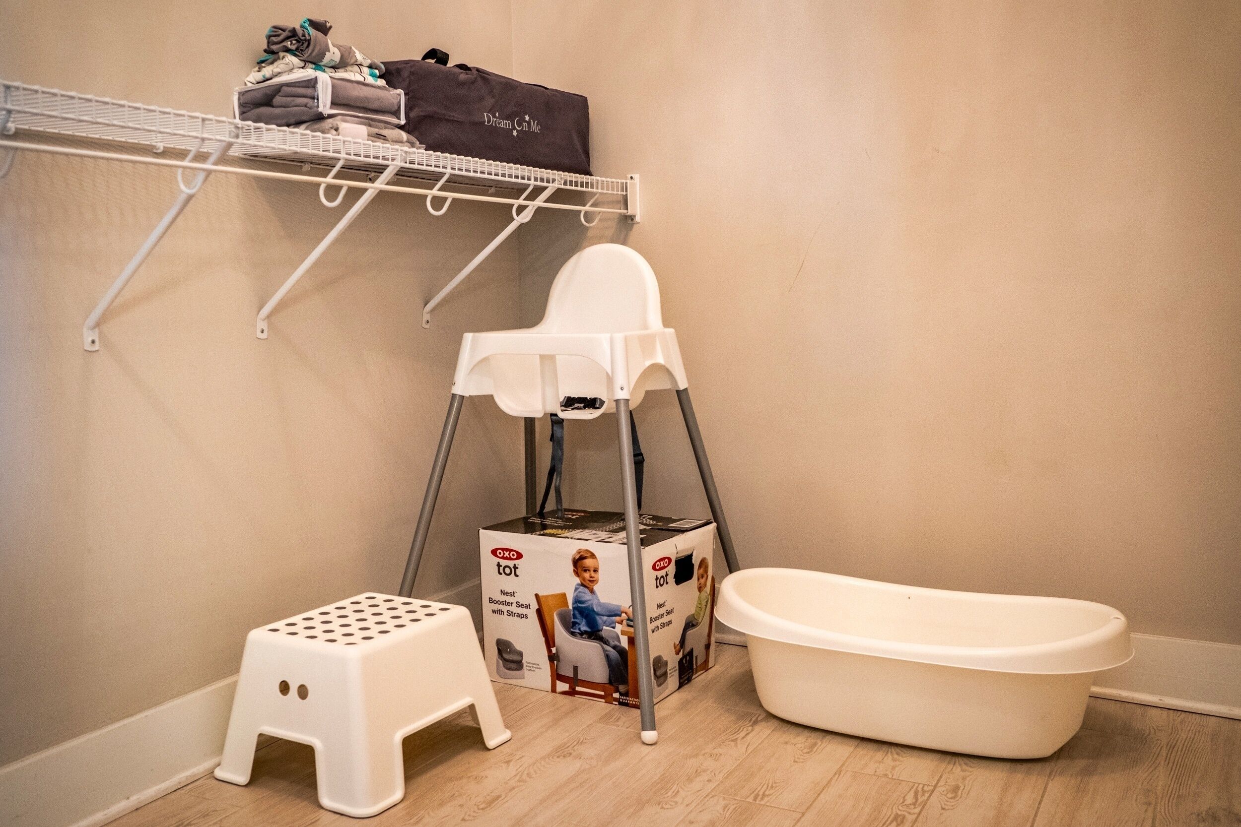 Un baño con una bañera blanca, un taburete blanco, una camita alta blanca y un estante con toallas dobladas.