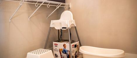 Un baño con una bañera blanca, un taburete blanco, una camita alta blanca y un estante con toallas dobladas.