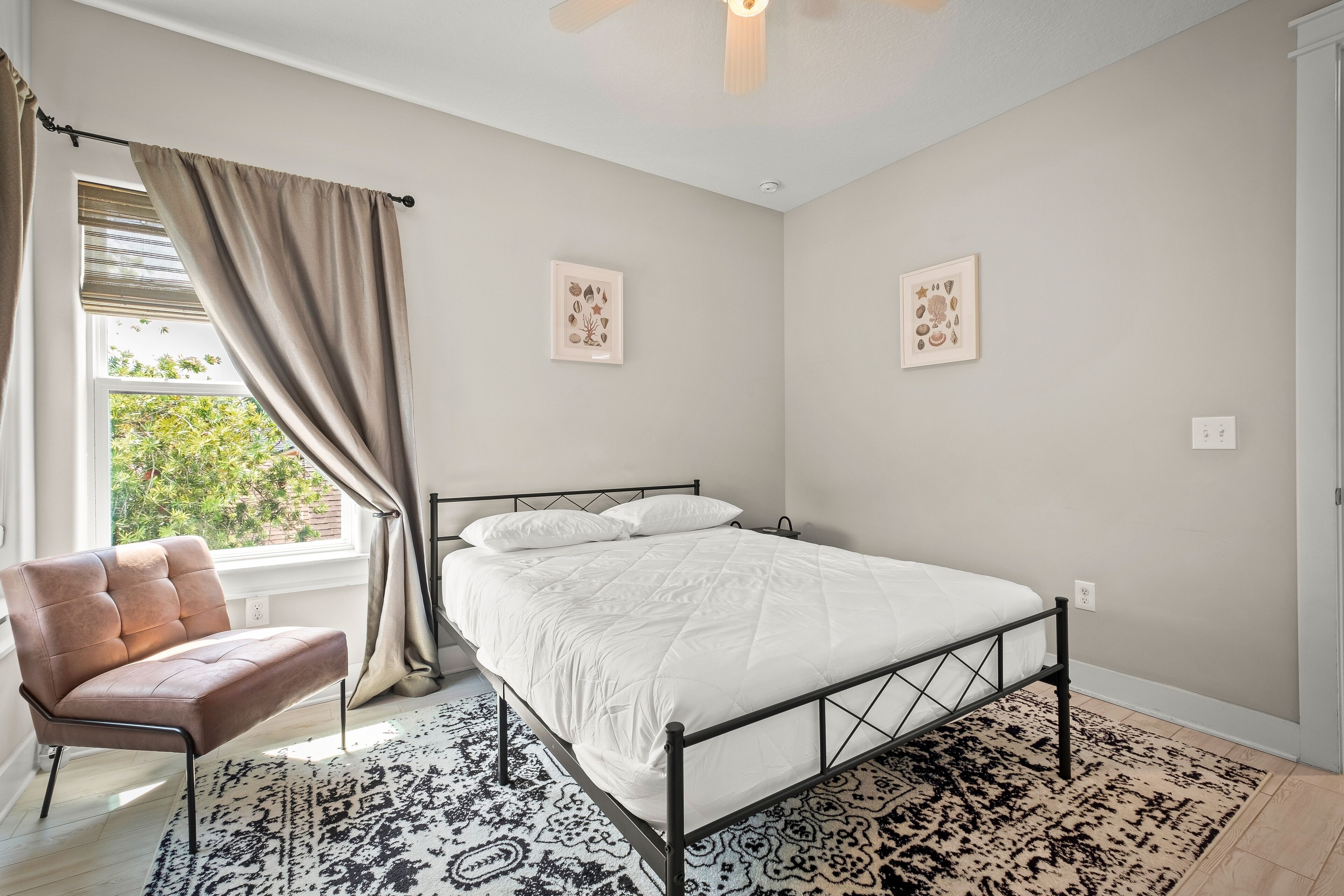 A bedroom with a bed, a chair, a window with curtains, and two wall-mounted pictures.