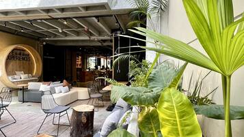 Een modern terras met een combinatie van banken en stoelen, omgeven door grote groene planten en een houten stronk.