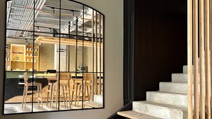 Un interior moderno con conductos expuestos, una escalera y un ventanal que refleja una zona de bar.