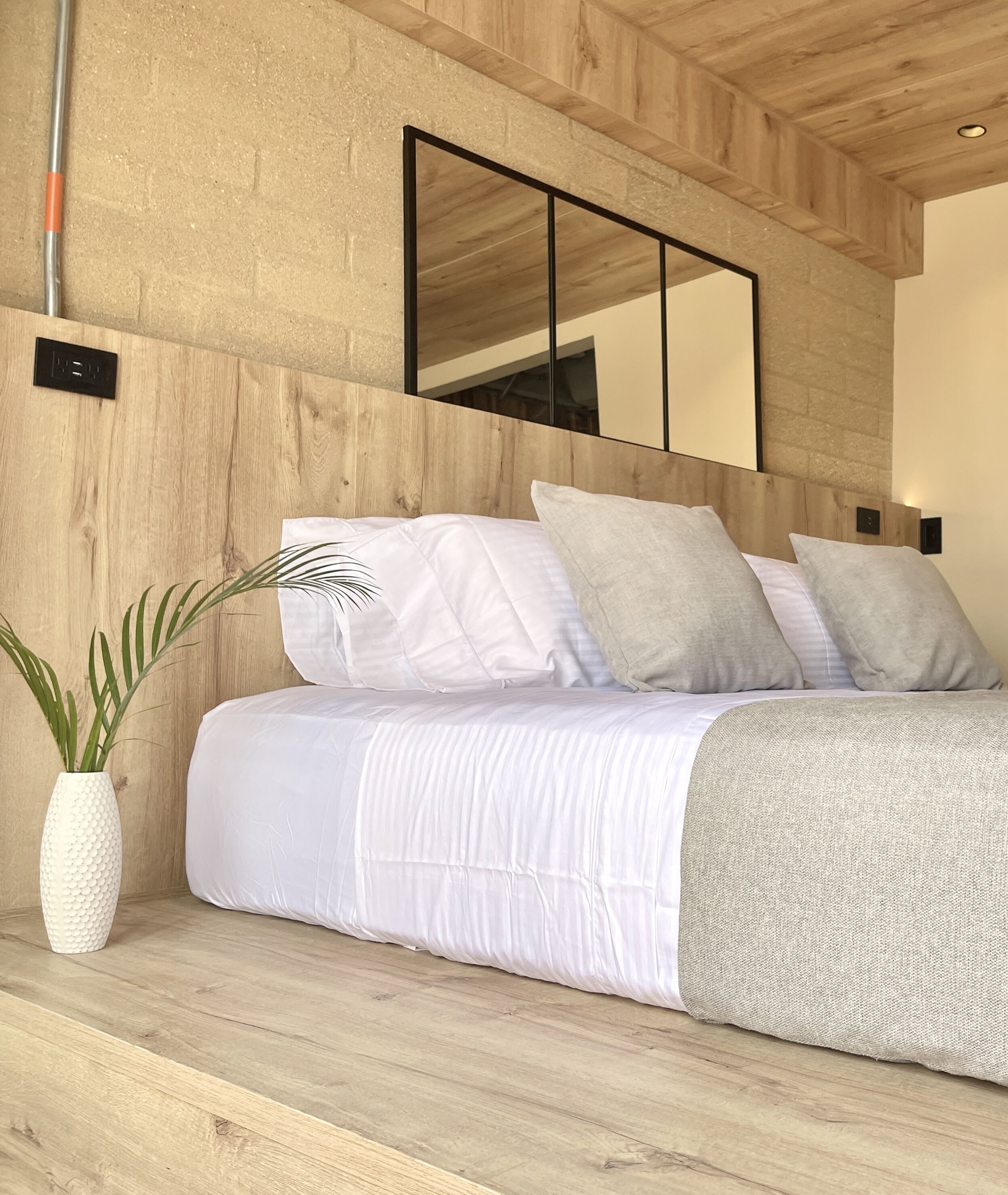 Un dormitorio moderno con cabecera de madera, cama con ropa de cama blanca y un espejo grande sobre la cama.