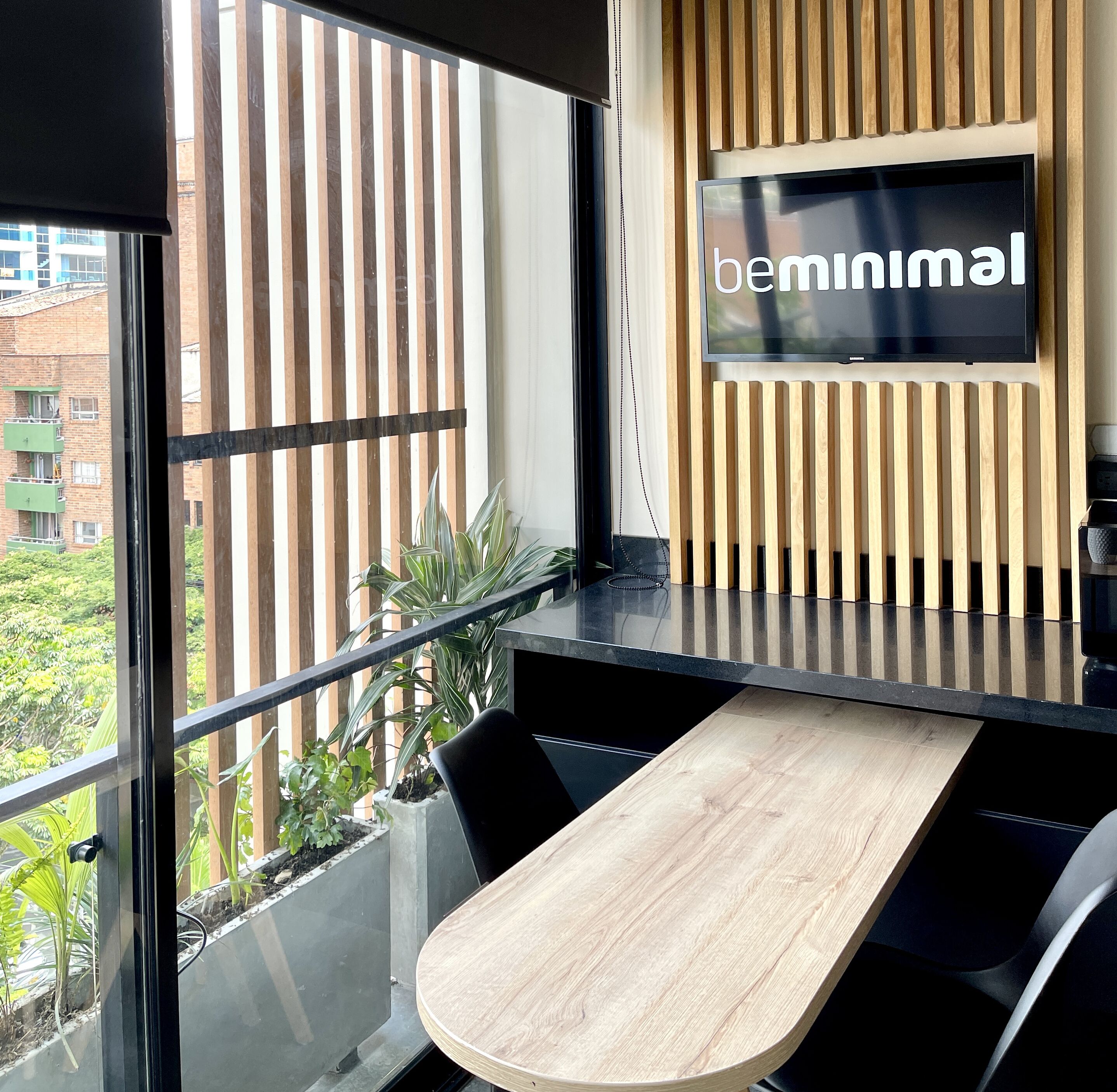 A modern office space with a large window, a wooden table, and a mounted TV displaying "bemminimal".