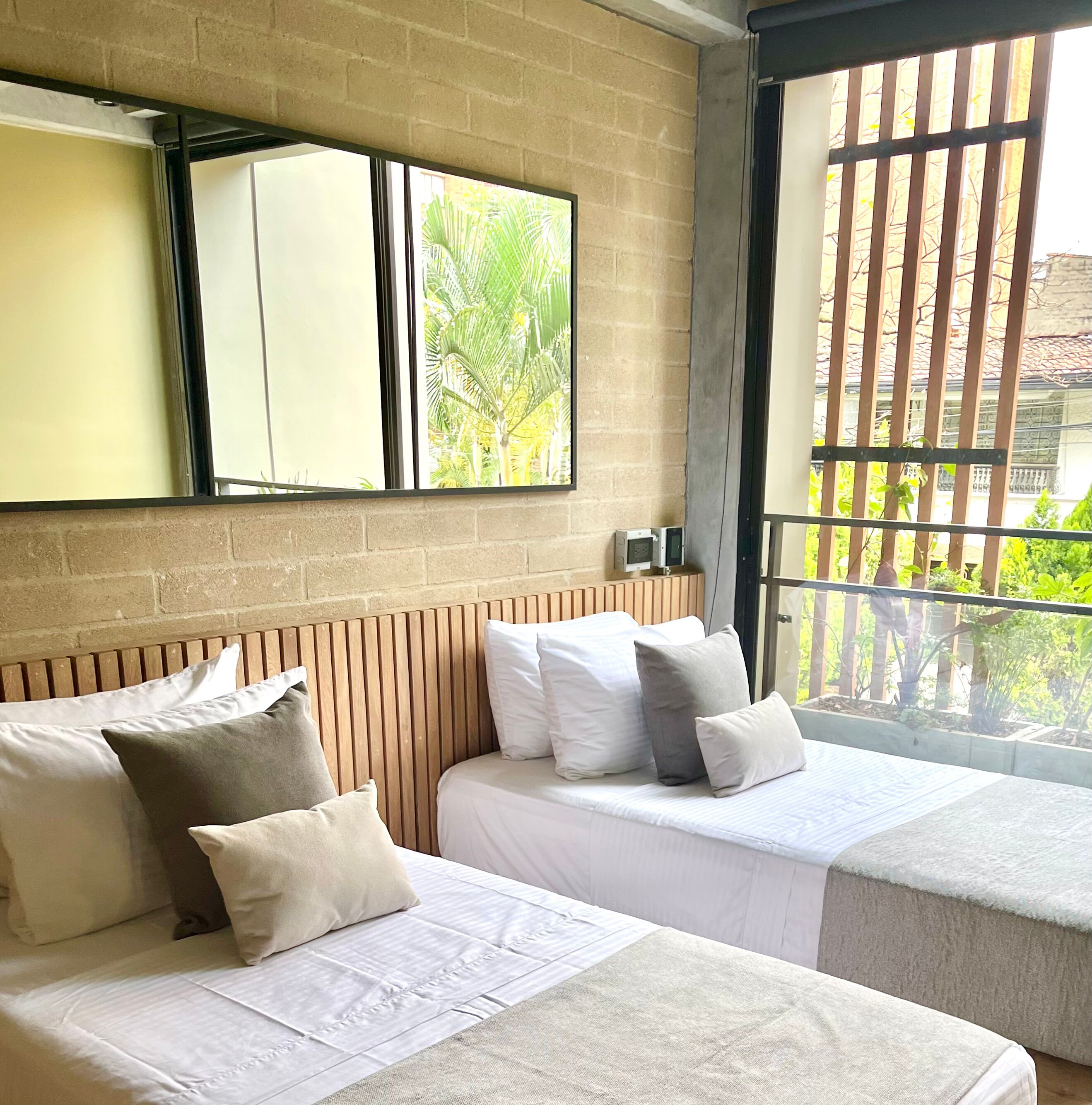 Habitació d'hotel amb dos llits, una finestra gran amb vista a vegetació i una paret de maó.