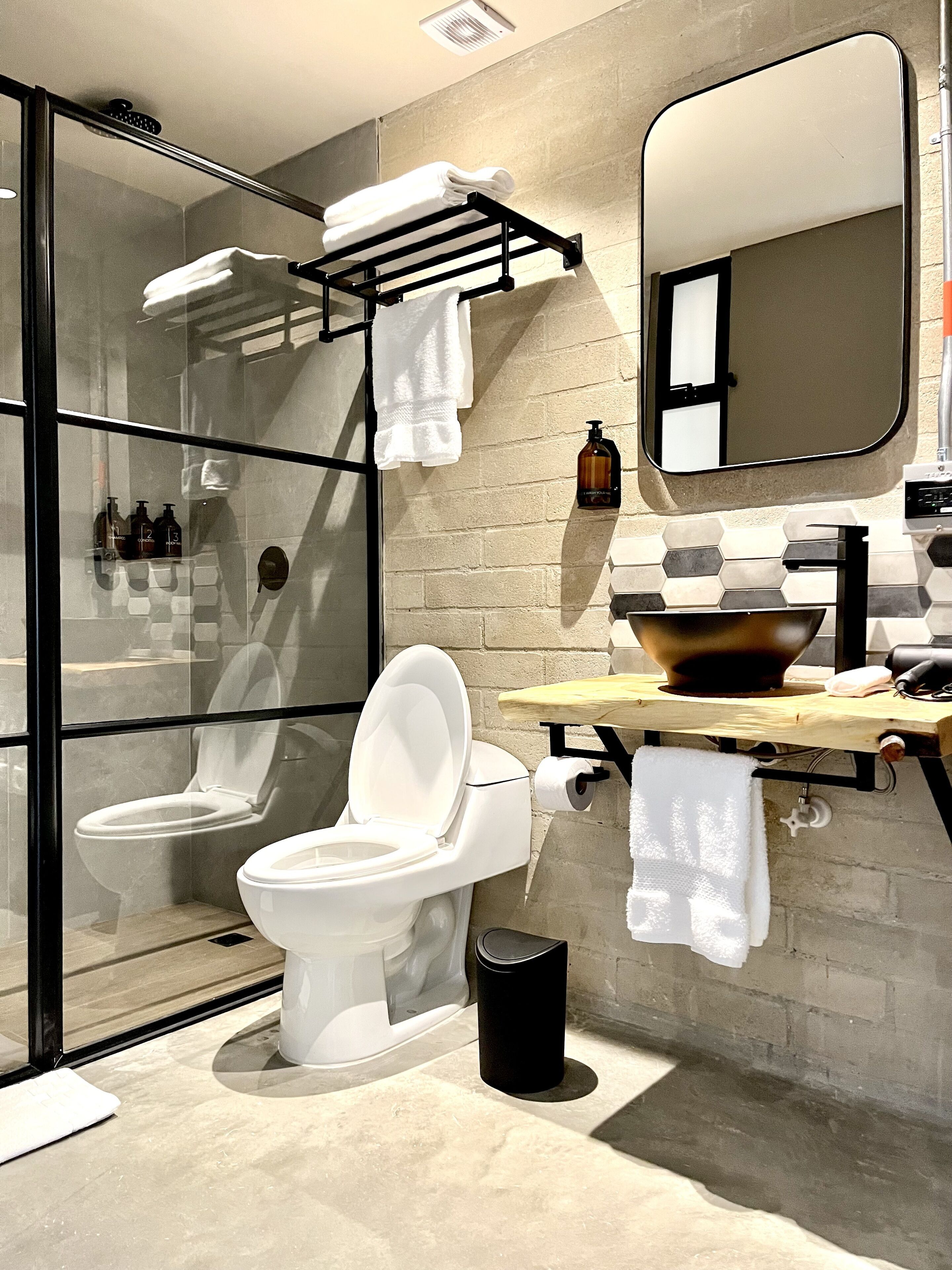 A modern bathroom with a glass shower enclosure, a white toilet, a sink with a wooden countertop, and a mirror.