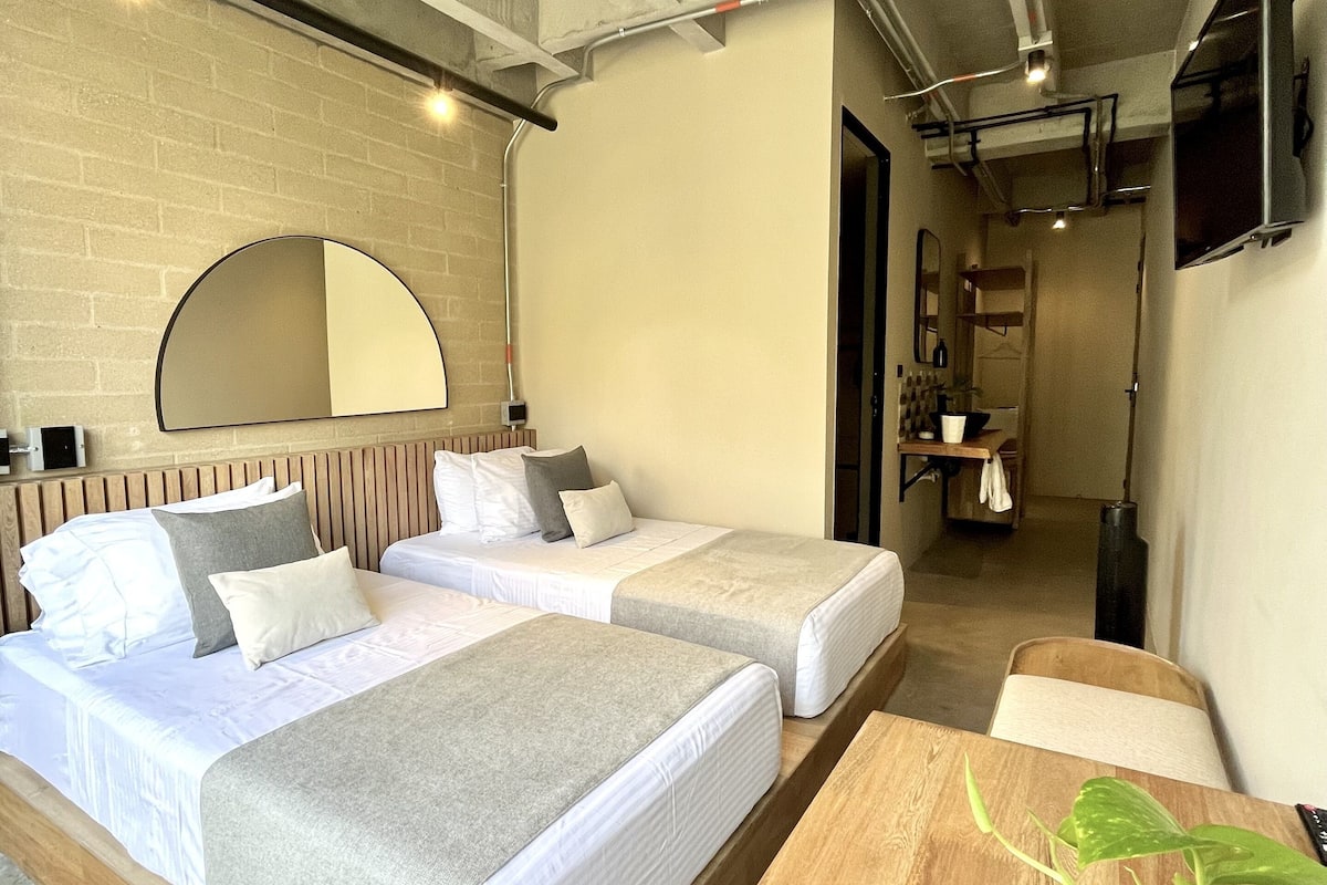 A modern room with two beds, a wooden table, and a large mirror on the wall.