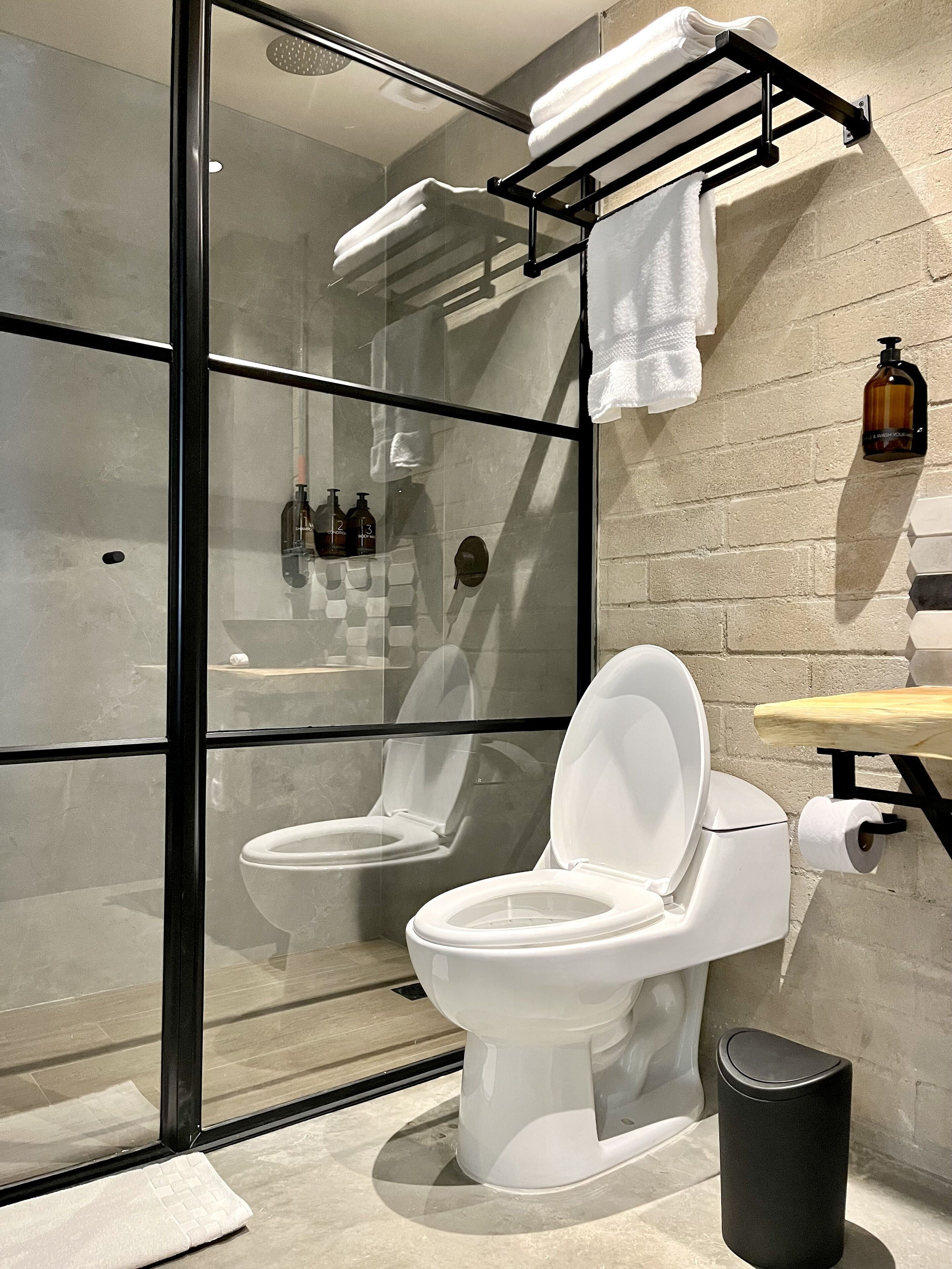 A modern bathroom with two toilets, a glass-enclosed shower, and a sink with a soap dispenser.