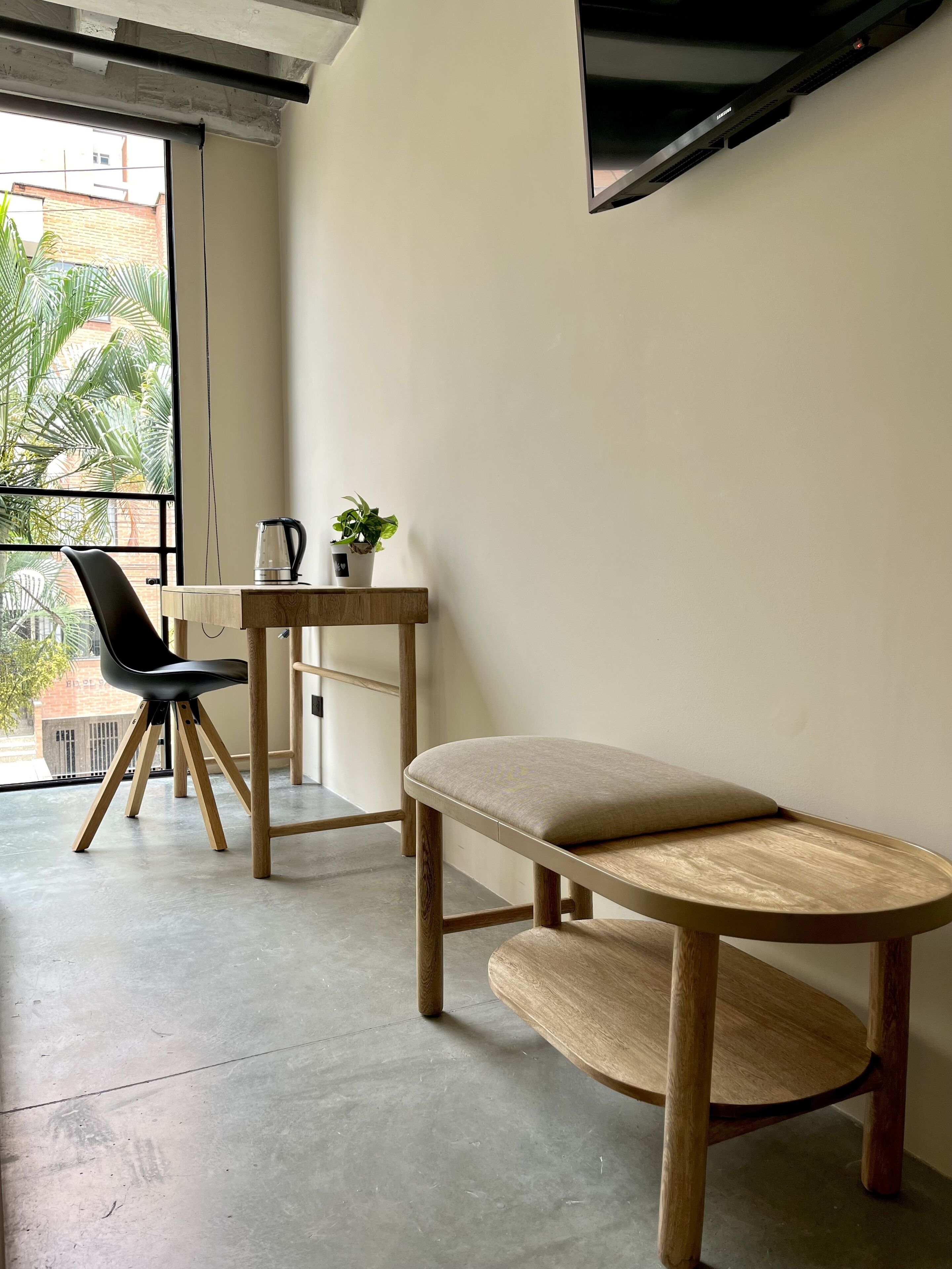 A modern, minimalist room with a concrete floor, a wooden table with a potted plant, a black chair, and a bench.