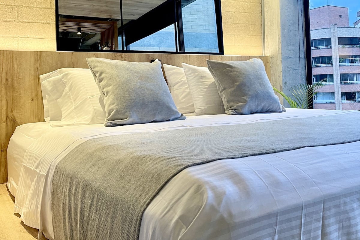 A neatly made bed with white bedding and a grey throw blanket.