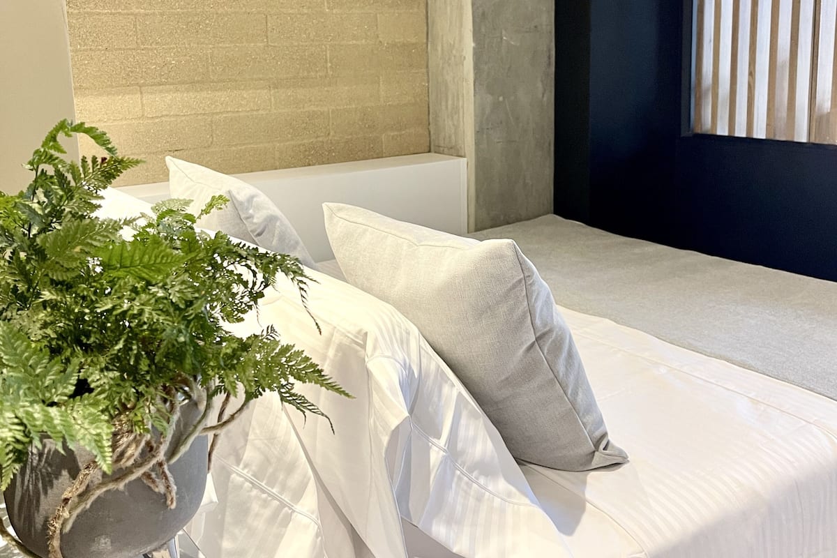 A modern bedroom with a bed, pillows, a potted plant, and a brick wall.