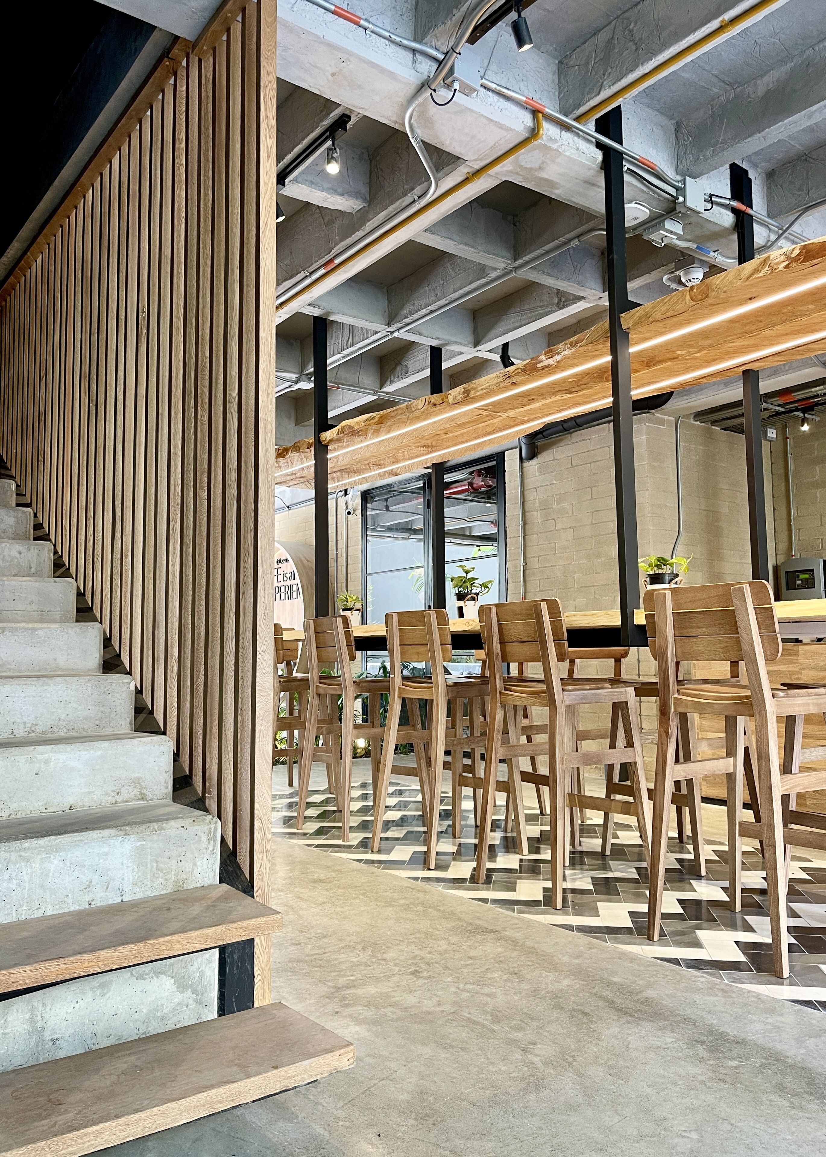 Un interior moderno con una escalera, paneles de madera y un comedor con sillas y mesas de madera.