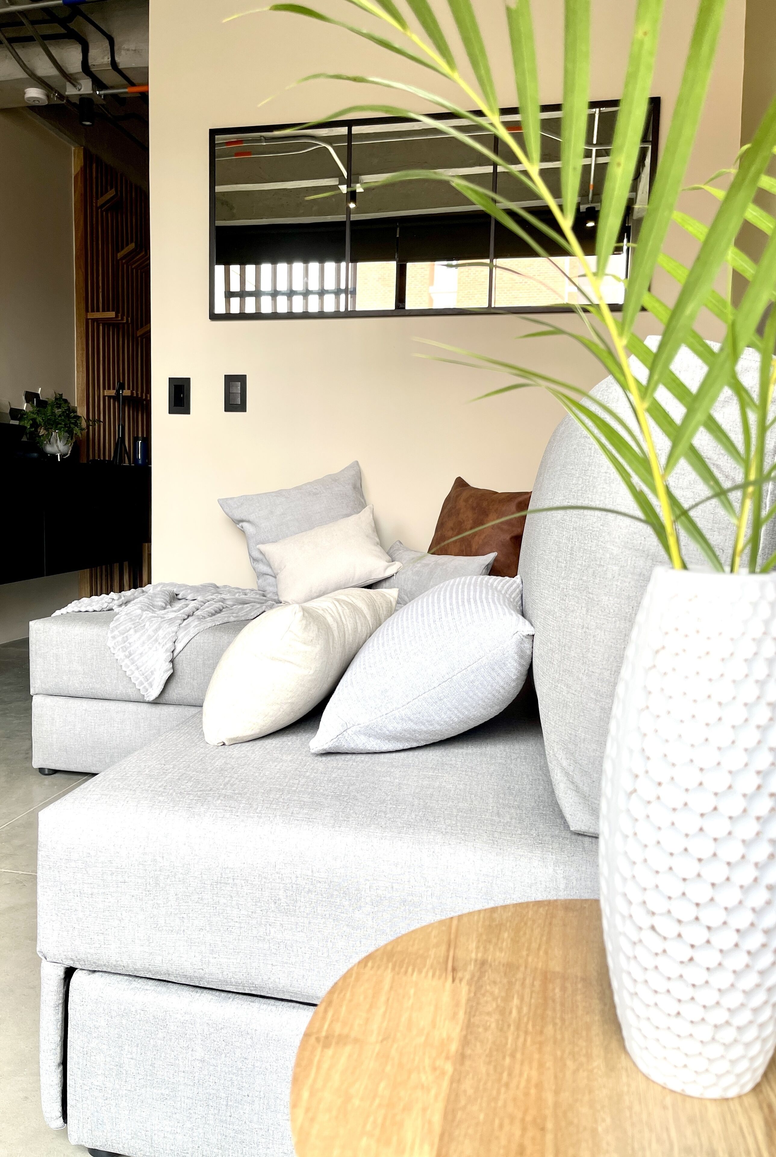 A modern living room with a grey sectional sofa, a white textured vase, and a wooden coffee table.