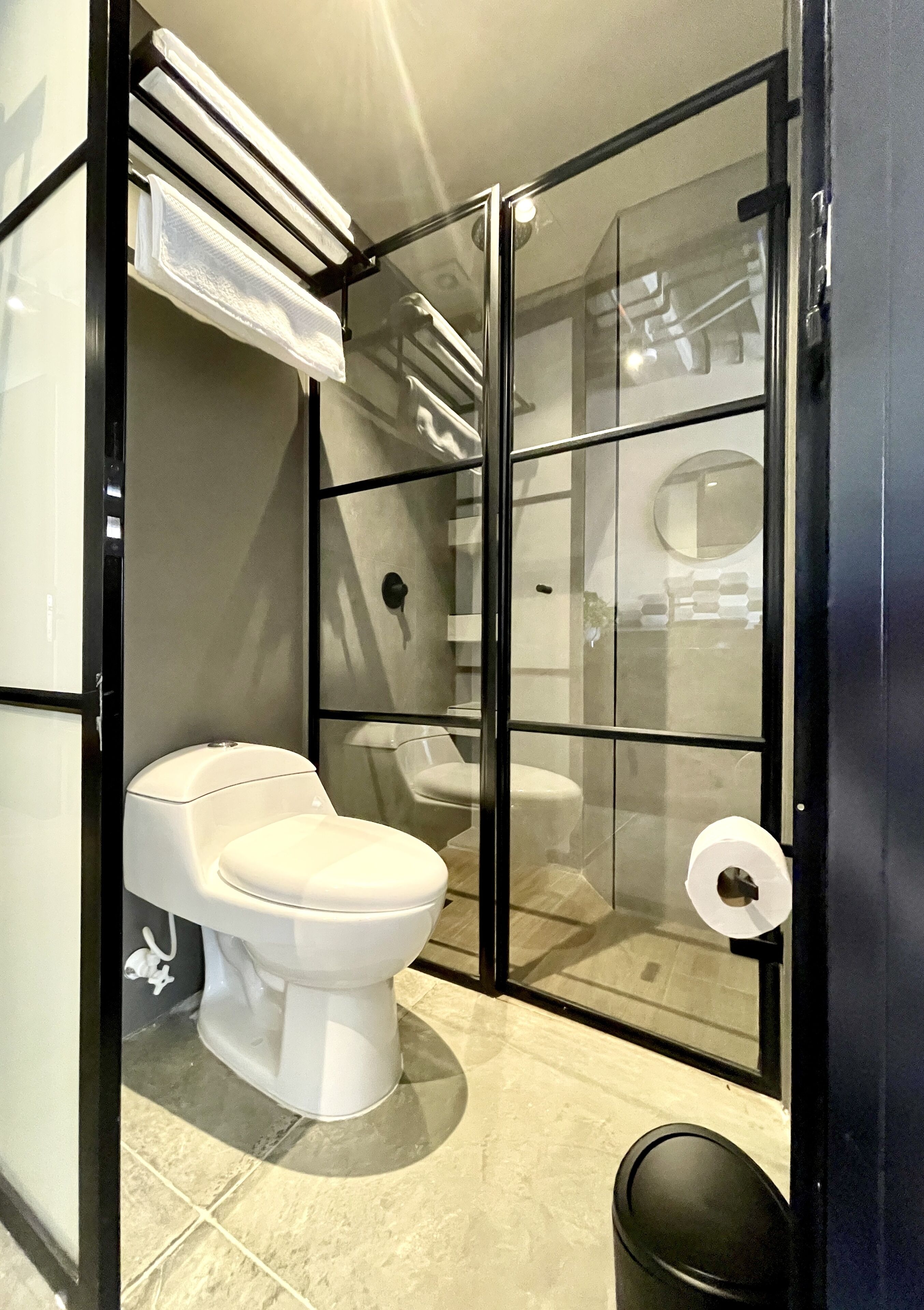 Un baño moderno con separador de vidrio, inodoro blanco, un cesto de basura negro y un perchero para toallas.