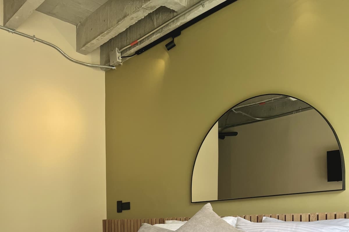 A neatly made bed with a white quilt and pillows, a large mirror above it, and a wooden headboard.