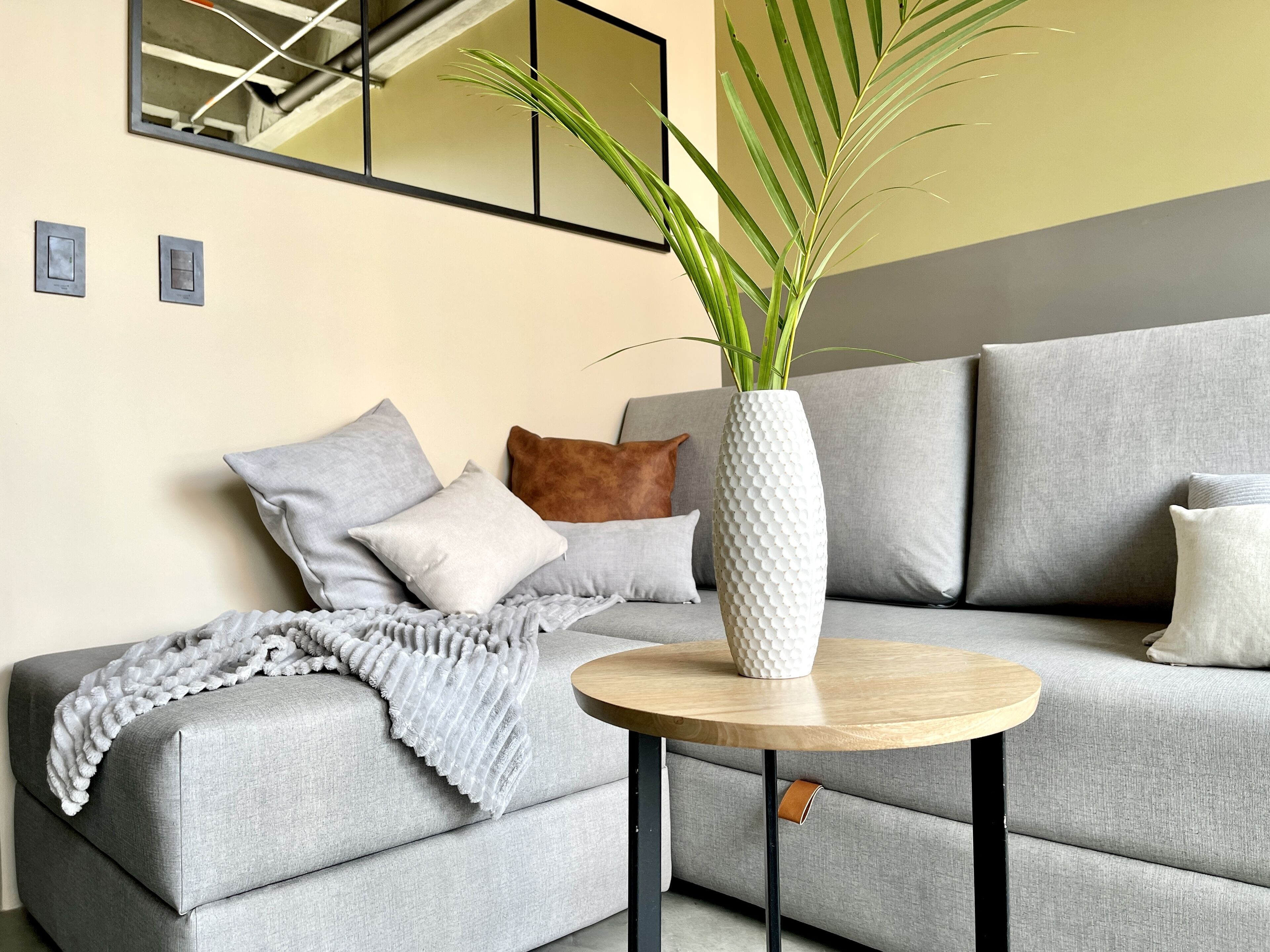 A modern living room with a grey sofa, a round wooden coffee table, and a white textured vase with green plants.