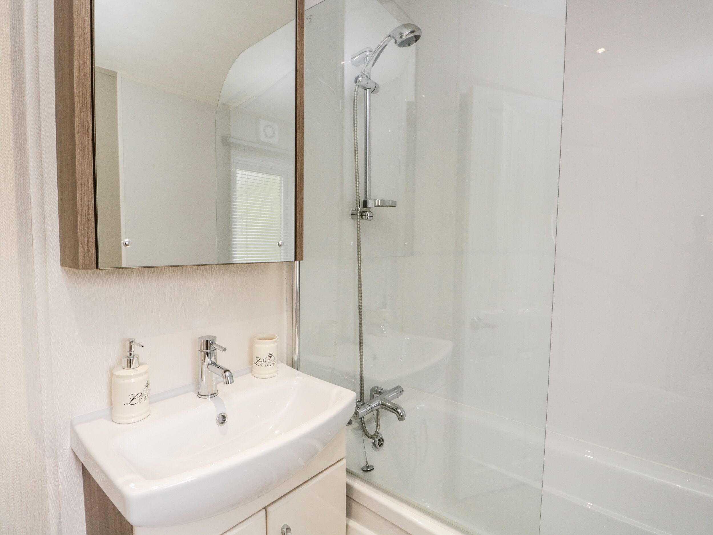 A bathroom with a white sink, mirror, and shower.