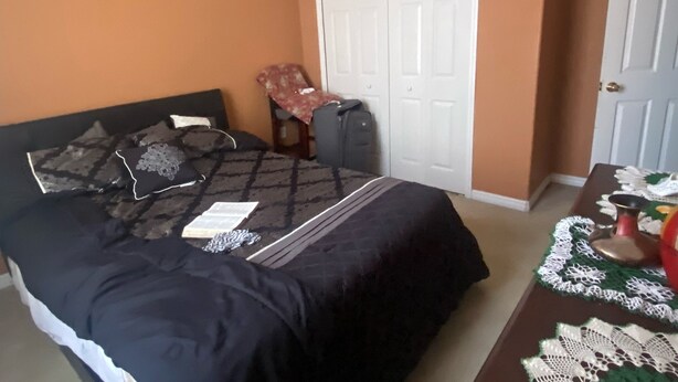 Quarto com cama, cadeira, mesa com toalha de renda e ventilador de teto.