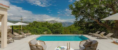 Area piscina con mobili in vimini, un tavolo rotondo e vista sulle montagne.