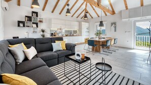 Een moderne woonkamer met een grijze modulaire bank, een zwarte salontafel en een eethoek met een houten tafel en stoelen.