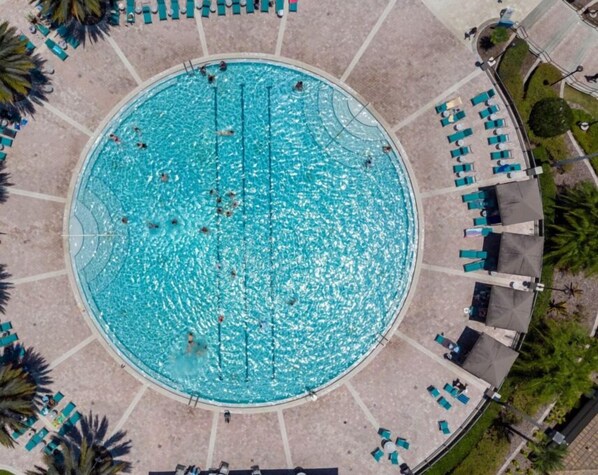 Une piscine circulaire entourée d’une terrasse, de chaises longues et de palmiers.