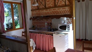 A kitchen with a brick wall, wooden beams, a white refrigerator, a microwave, and a coffee maker. - Gite in the mountains (Seix)