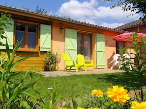 Una casa con jardín, un patio con sillas y un paraguas rojo.
