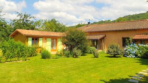 A two-story house with a tiled roof, surrounded by a well-maintained lawn and various shrubs. - Gite in the mountains (Seix)