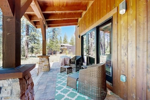 Relax on the covered patio, surrounded by the serene forest, with a sofa, chairs, and table.