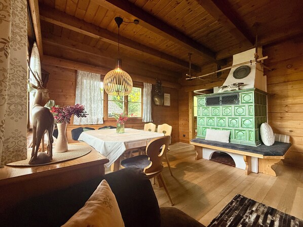 A wooden cabin interior with a dining table, chairs, a bench, a green cabinet, and a deer sculpture.