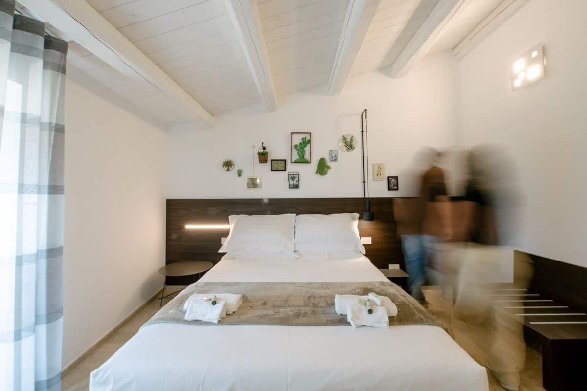 Ein Hotelzimmer mit einem großen Bett, einem Nachttisch, einem kleinen runden Tisch und einer Wand mit gerahmten Bildern und Pflanzen.