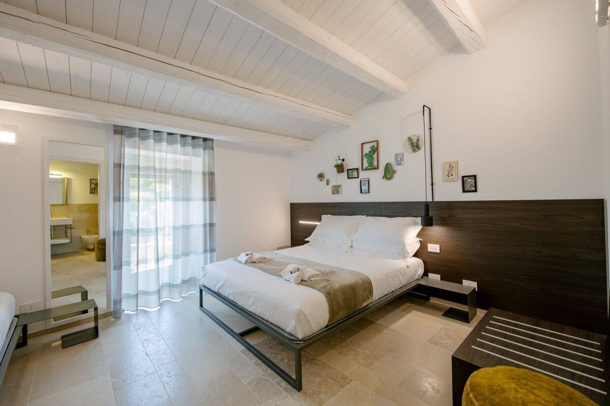 Ein modernes Schlafzimmer mit einem Bett, Nachttischen, einer Bank und Blick ins Badezimmer.