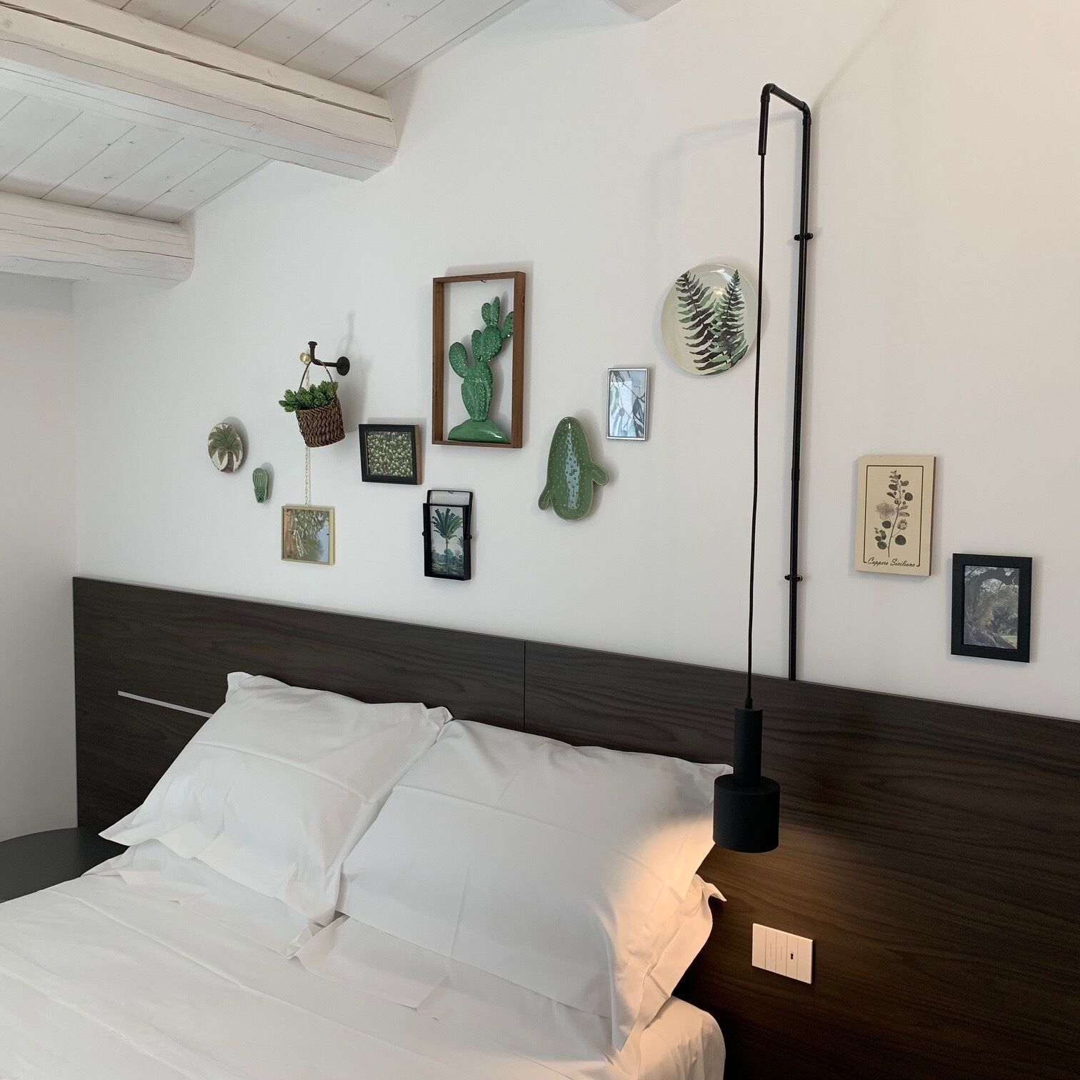 A bedroom with a bed, a wall-mounted lamp, and various framed botanical prints and sculptures.