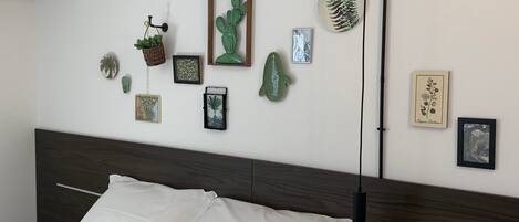 A bedroom with a bed, a wall-mounted lamp, and various framed botanical prints and sculptures.
