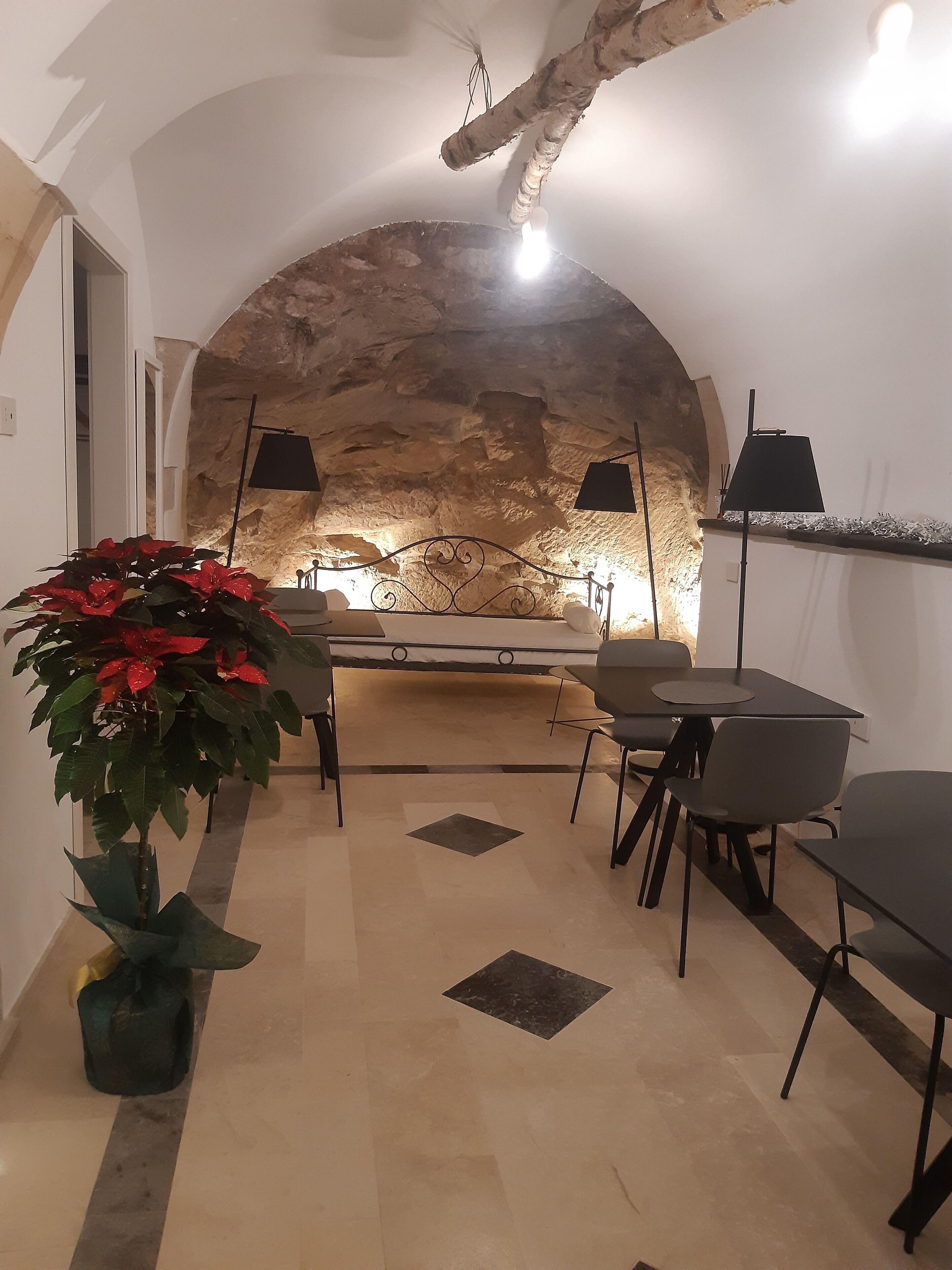 Um interior acolhedor com parede de pedra, área de jantar com mesa e cadeiras, e um vaso com flores vermelhas.