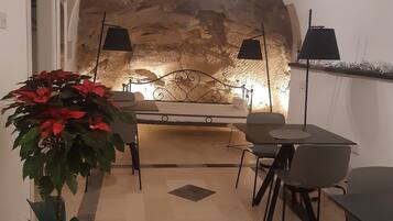 Um interior acolhedor com parede de pedra, área de jantar com mesa e cadeiras, e um vaso com flores vermelhas.