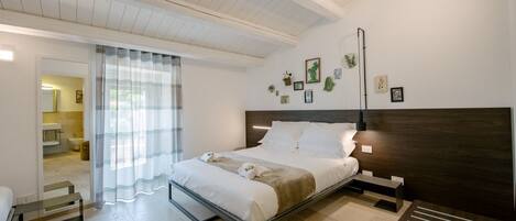 A modern bedroom with a bed, bedside tables, a bench, and a view of the bathroom.