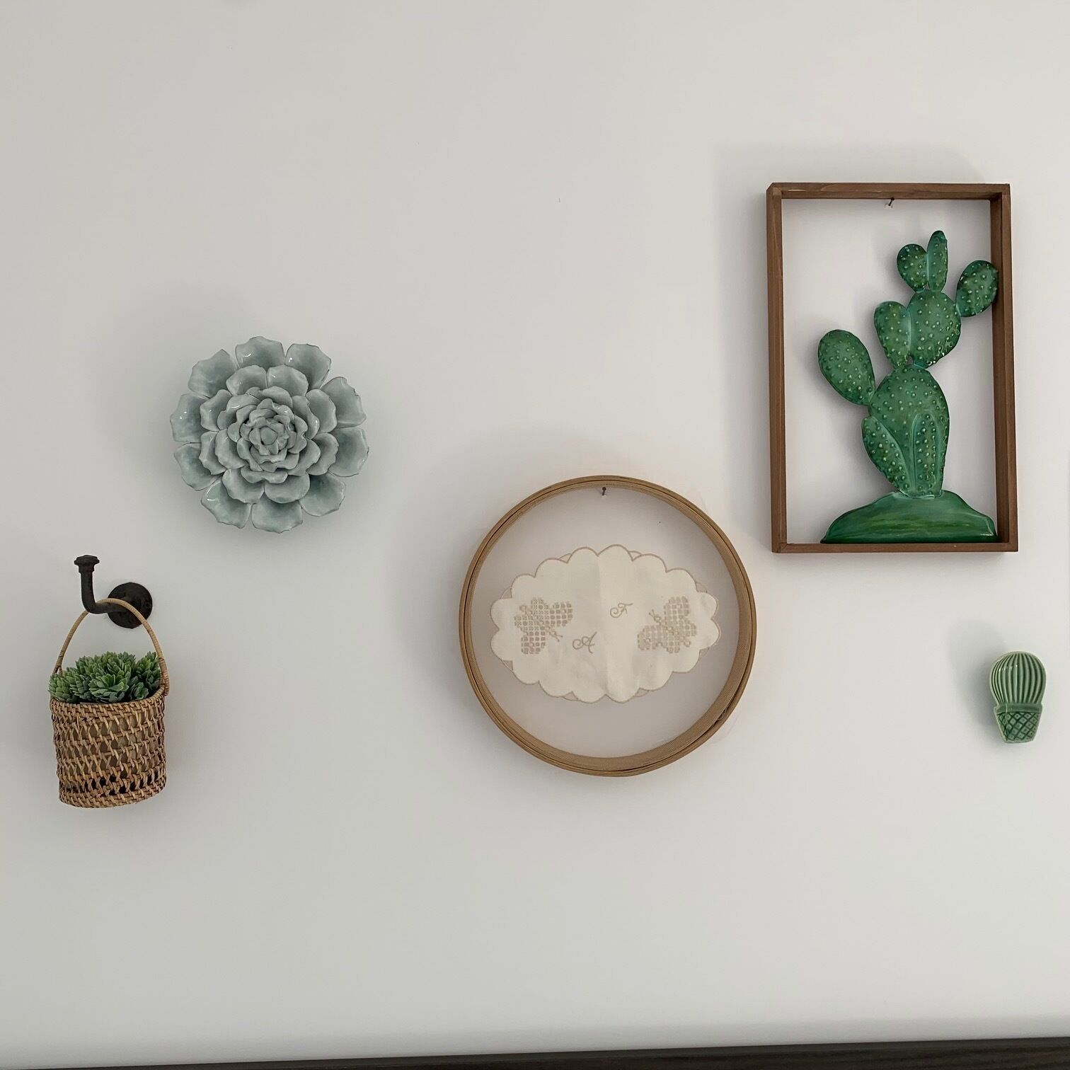 A wall with various decorative items including a framed cactus, a woven basket with a plant, a grey flower, and a circular frame with a cloud design.